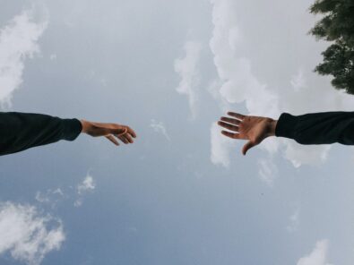 Two hands reaching out in front of a cloudy blue sky
